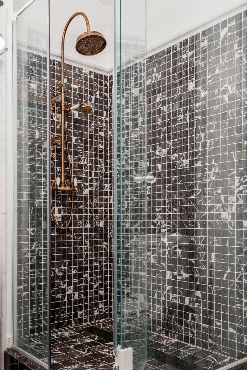 Shower enclosure between dark tiles with gold hardware